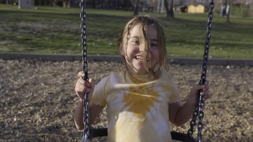 Little Blonde Girl Enjoying the Swing Outdoors in the Playground in Summertime