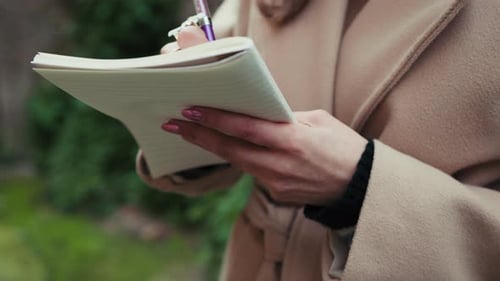 Woman's hands writing in notebook outdoors