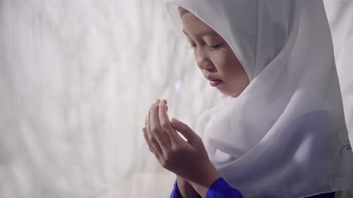 Niña musulmana asiática que lleva un hiyab hace un gesto de oración