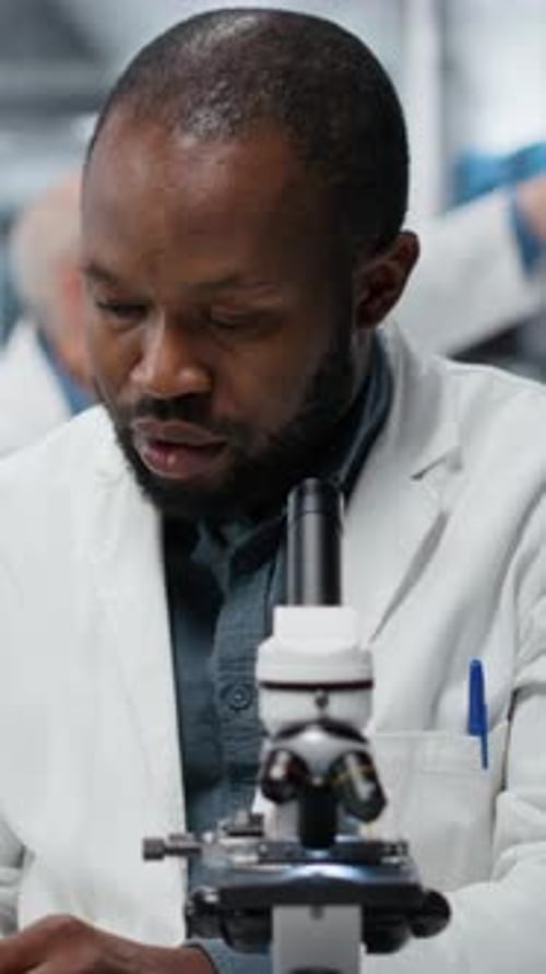 Scientist examines specimen slide using microscope in laboratory