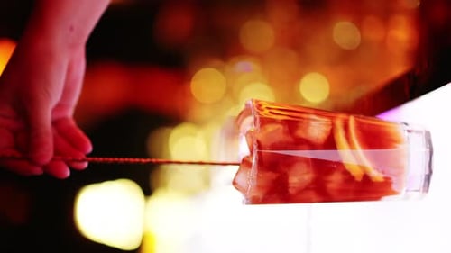 Barman making and stirring cocktail with whiskey liquor alcohol at the bar at night with red neon li