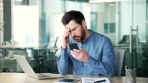 Stressed Man Looking at Phone in Modern Office