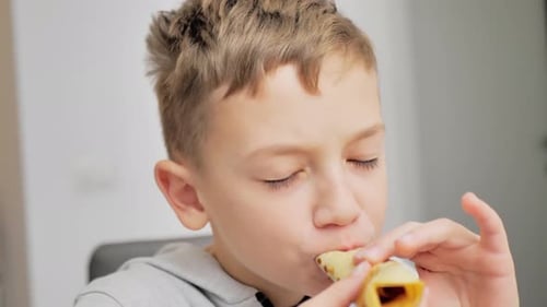 A Boy Eats Pancakes with Jam in a White Kitchen