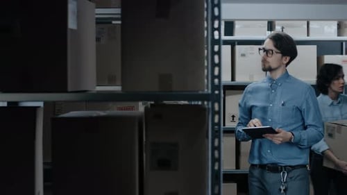 Warehouse Inventory Manager Uses Tablet Computer to Check Stock on Shelves. Rows Of Shelves with Ca