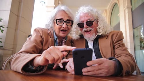 Senior Couple Enjoying Smartphone at Outdoor Cafe