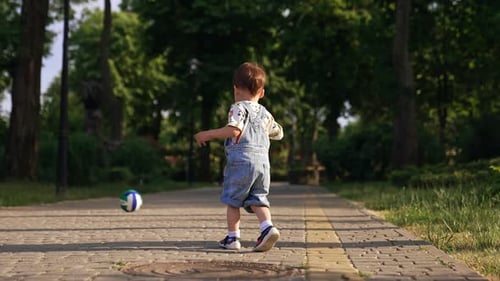 Little boy notices a ball on the paved road. Baby boy runs to the toy and picks it up.