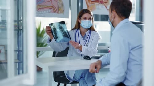In Modern Hospital Young Woman Doctor with Medical Mask Explain Xray Chest Result Speaking with