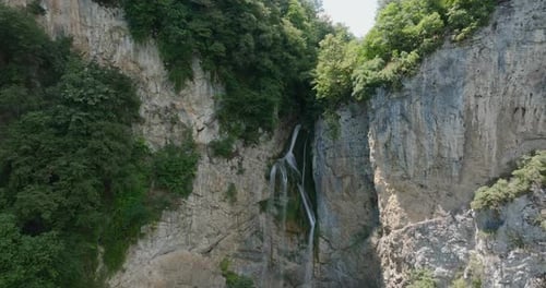 A waterfall falling from a stone cliff in the forest. Aerial view of nature.