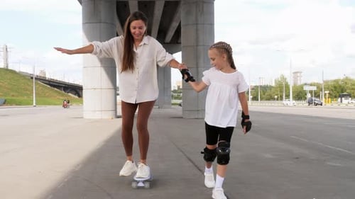 Woman Skateboarding with Girl Under Highway Overpass