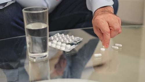 Man with Pills and Water on Glass Table