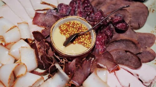 Planche de charcuterie gastronomique avec assortiment de charcuteries, tranches fumées et sauce aux graines de moutarde servie