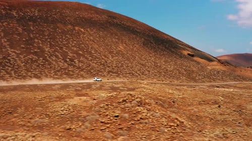 White Car Driving Alone Travel on Empty Dirt Road Freeway Through Desert Volcanic Landscape at