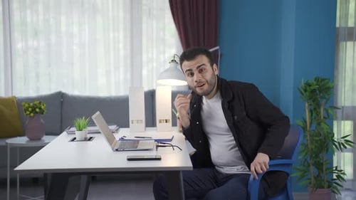 Young Man Thinking at Desk with Laptop