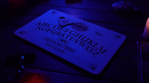Close Up Video of a Wooden Ouija Board on a Table Surrounded By Candles Candlesticks and Other