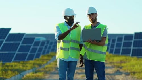 Two Engineers with Laptop on the Solar Farm in Special Uniform Standing Discuss the Installation of