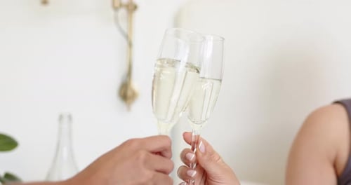 Deux mains font tinter des flûtes, la gauche s'éloignant tandis que la droite tient, célébrant dans une pièce pâle