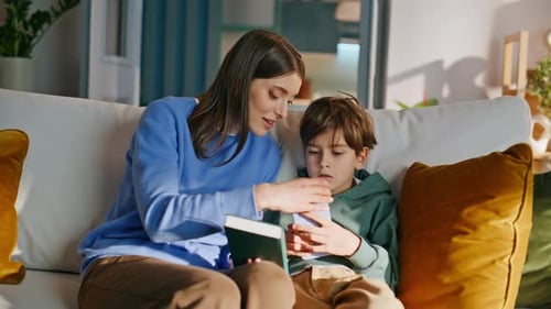 Woman Reads Book to Boy on Couch at Home
