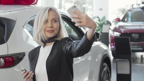 Joyful Woman Capturing Selfies with Her New Car Keys at the Dealership