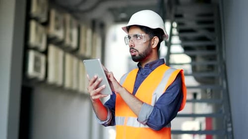 Professional engineer wearing safety helmet and vest standing at the factory and working