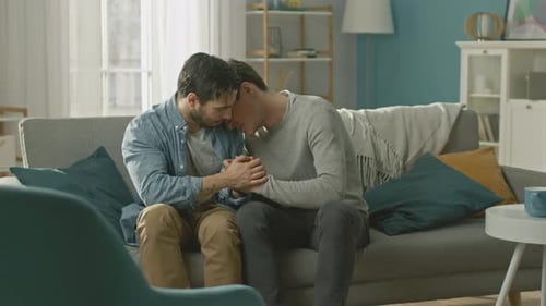 Loving Young Gay Couple Embracing on Couch at Home