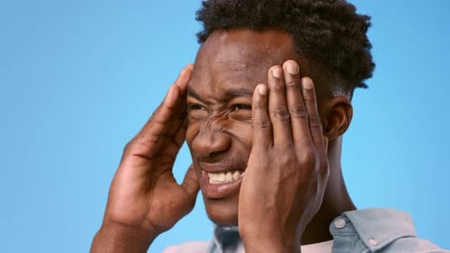 Junger Afroamerikaner leidet unter Kopfschmerzen vor blauem Hintergrund