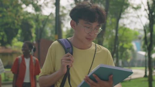 Asian College Student Walking in Park with Workbook
