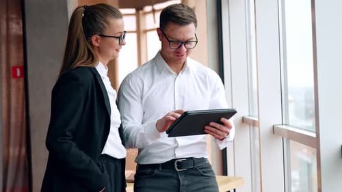 Positive Kollegen kommunizieren bei der Arbeit. Mann benutzt I-Pad und eine Frau, die neben ihm steht, spricht mit dem Mann
.