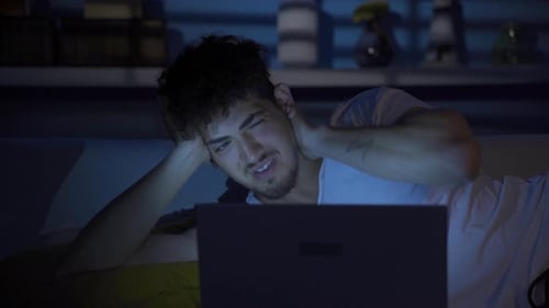 Tired Man Lying in Bed Using Laptop at Night