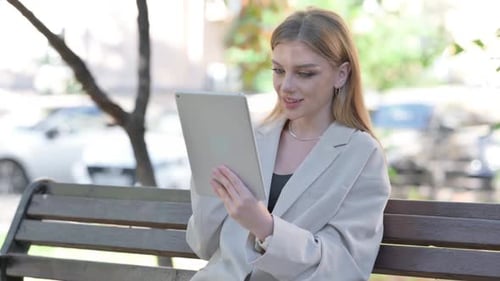 Young Businesswoman Doing Video Chat on Tablet while Sitting on Bench on a Bench