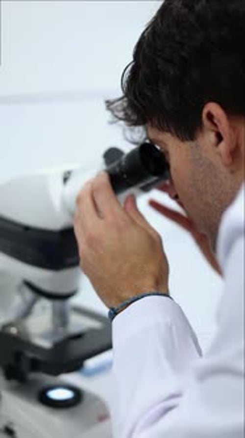vertical Scientist analyzing samples under microscope in laboratory
