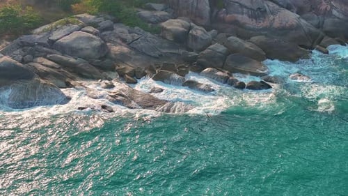 Aerial drone view of foamy waves breaking on a rocky shore.