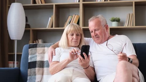 Senior Couple Enjoys Smartphone on Couch at Home