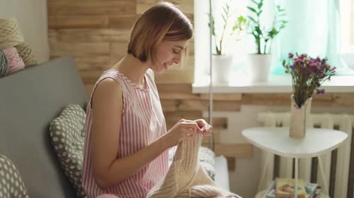 Woman Sitting On Couch And Knitting Wool Yarn In Home Workshop. Smiling Woman Knitting Needles Wo...