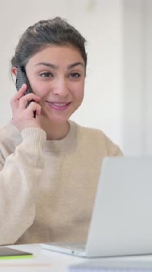 Smiling Woman Using Phone at Desk with Laptop