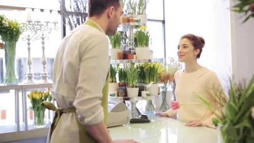 Happy florist man showing flowers to woman at flower shop during a sale