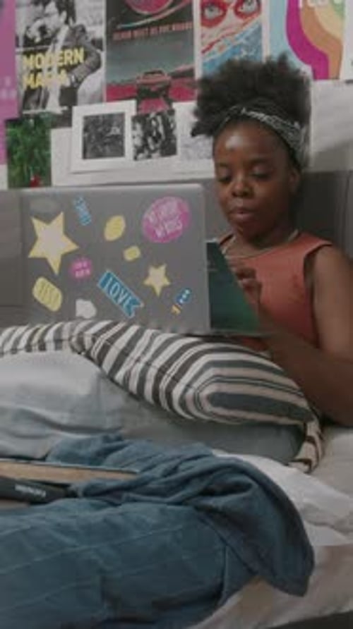 Young Woman Uses Laptop and Phone in Bedroom