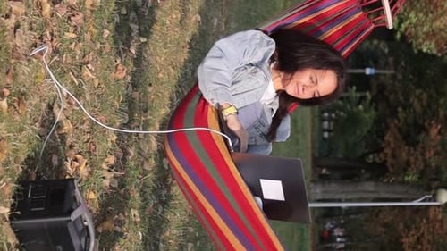 Uma jovem programadora está trabalhando em um laptop debaixo de uma árvore e carregando-o de um portátil