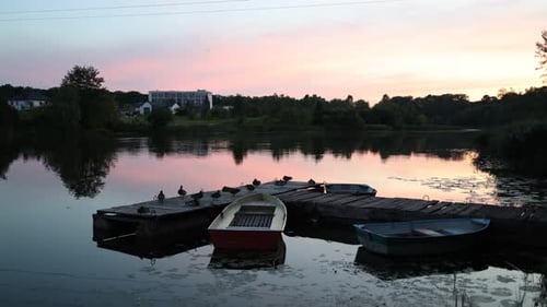 Beautiful sunset on the river, lake. Multi-colored boats sway on the water at the pier.