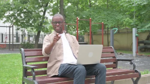 Hombre africano apuntando directamente al espectador con una computadora portátil al aire libre