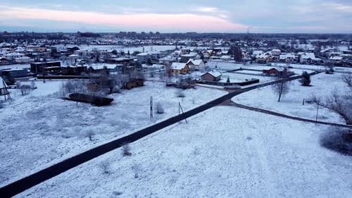 Sunset aerial landscape of a Baltic winter village covered in Snow, establishing drone panning view