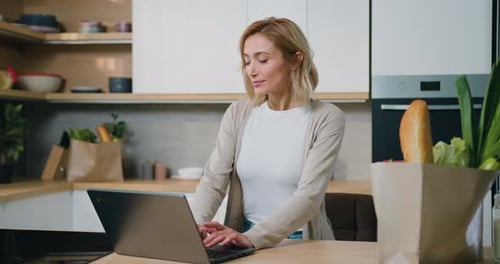 Woman Typing on Laptop in Bright Kitchen