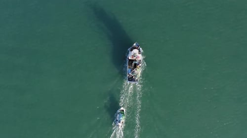 Large Fishing Boat dragging a smaller boat heading out to sea.
