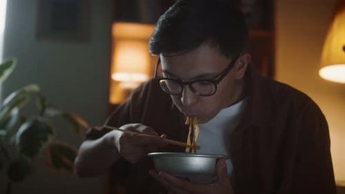 Young Adult Eats Noodles at Home in Evening