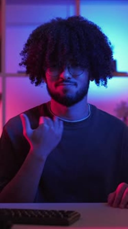 Man with Curls Sits Under Neon Lighting