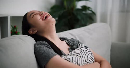A young woman sits smiling and laughing while thinks of something funny.