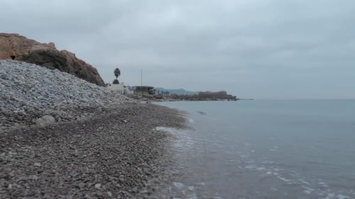 low drone shot glides forward along rocky shoreline of sea, capturing rugged beauty of coastline on