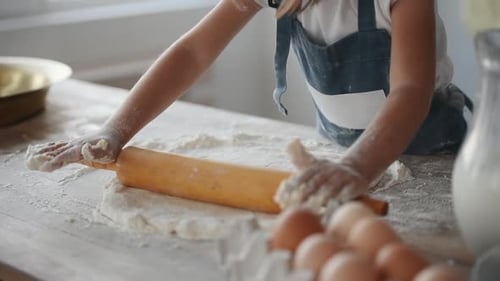 Close up view of kid in chef uniform that kneading the dough by wooden tool on the kitchen