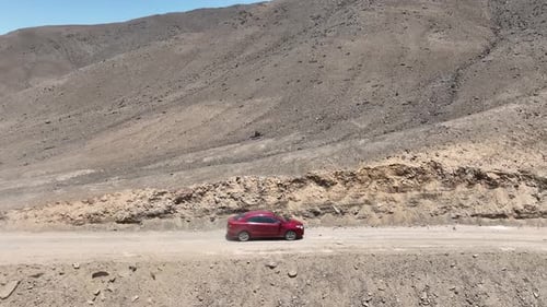 Fotografía aérea de un automóvil rojo en movimiento en un páramo de Perú en una polvorienta y seca carretera desértica a lo largo del