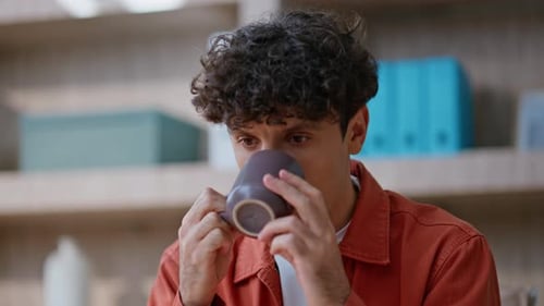 Man with Curly Hair Drinks Coffee Indoors