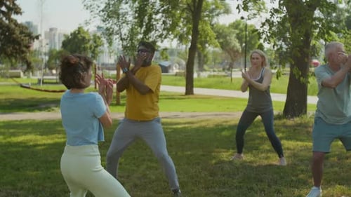 Group of Retired People Repeating Arm Movements after Qigong Trainer in Park